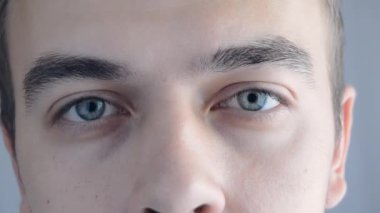 Man 'in yüzüne yakın çekim. Güzel mavi gözleri olan çekici bir çocuk. Beyaz erkek model, mavi, yeşil, gri gözlü, makro yakın plan.