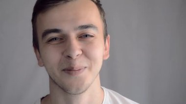 Yakın çekim portresi genç yakışıklı Avrupalı görünümlü mavi gözlü adam kameraya bakıyor ve gülümsüyor.