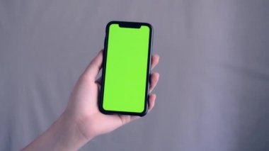 Hands holding cell phone with green screen on a grey background
