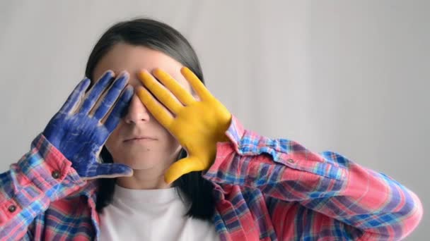 Young Scared Woman Painted Hands Blue Yellow Hides Her Eyes — Vídeo de Stock