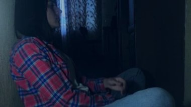 Mutsuz genç esmer kadın karanlık bir odada oturur ve duvara yaslanır. Sosyal sorun kavramı. Depresyon, bağımlılık, aile içi şiddet