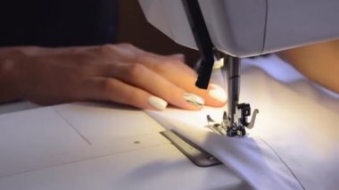 Needle for sewing machine in motion. The close-up of the sewing machine needle quickly moves up and down. The seamstress sews white fabric in the sewing workshop. The process of sewing the fabric.