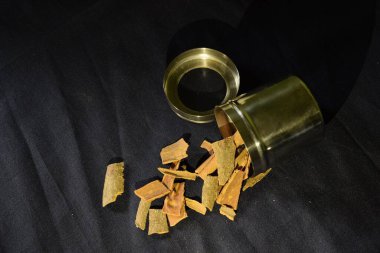 Açık bir baharat kabından dökülen tarçın, siyah arkaplanlı.