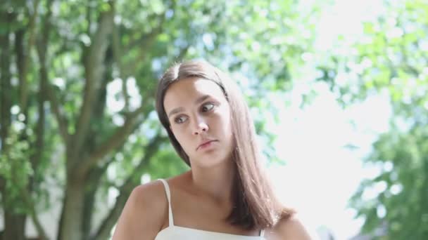 Pretty young brunette female long disheveled hair wind goes away green trees — Stock Video