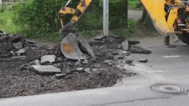 Sarı kazıcı kovası eski gri asfaltı yaz gününden kaldırıyor.