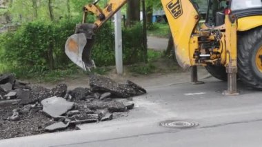 Sarı kazıcı kovası eski gri asfaltı yaz gününden kaldırıyor.