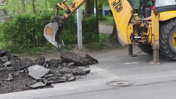 Balde escavadeira amarela remove pedaços de asfalto cinza velho do dia de verão estrada — Vídeo de Stock