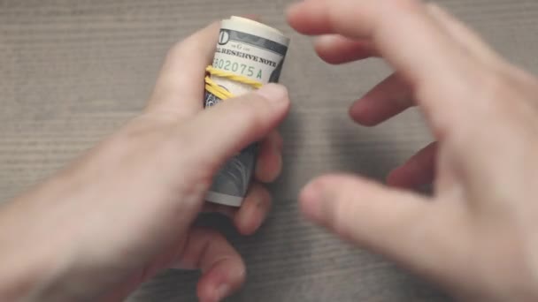 Mãos colocando elástico amarelo em um rolo de notas de cem dólares — Vídeo de Stock
