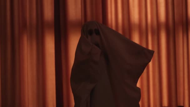 Niño pequeño en traje de fantasma de halloween blanco en hoja de cama fondo naranja — Vídeos de Stock