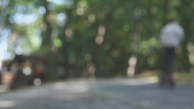 Bulanık yeşil halk parkı, ağaçlar gri yollar arka plandaki insanları dağıtıyor.