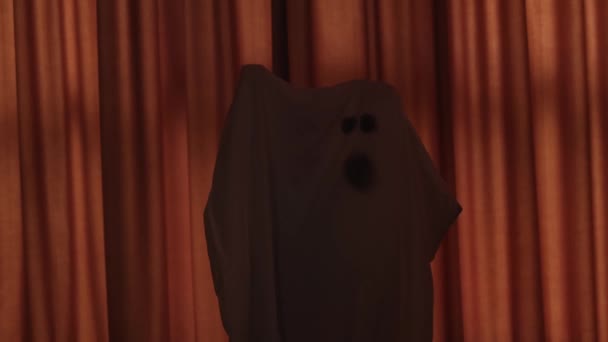 Niño pequeño en traje de fantasma de halloween blanco en hoja de cama fondo naranja — Vídeos de Stock