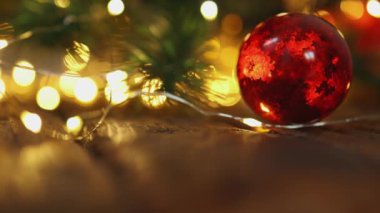 Kırmızı süslemeli cam top yeşil Noel ağacında bulanık ışıklarla asılı.