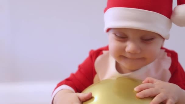 Портрет кавказский ребенок малыша Санта костюм красный шапочка играет золотой шар — стоковое видео