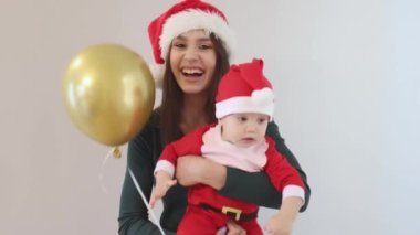 Genç, esmer, uzun saçlı, yeşil tişörtlü bir anne ve yedi ay boyunca Noel Baba 'nın kırmızı kostümlü şirin bebeği ve altın şapkalı yardımcıları olan beyaz bir Noel ailesi. Gülen neşe