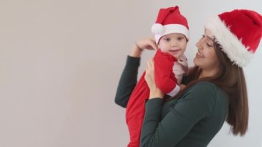 Gülümseyen beyaz tenli, esmer, uzun saçlı, yeşil tişörtlü, elinde tatlı bir bebek olan anne. 9 ay boyunca Noel Baba 'nın kırmızı kostümlü bebeği.