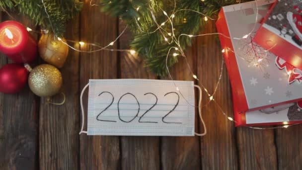 Κόκκινο χριστουγεννιάτικο κερί κουτί δώρου έλατο προστατευτικό μάσκα 2022 φώτα ξύλινο τραπέζι — Αρχείο Βίντεο