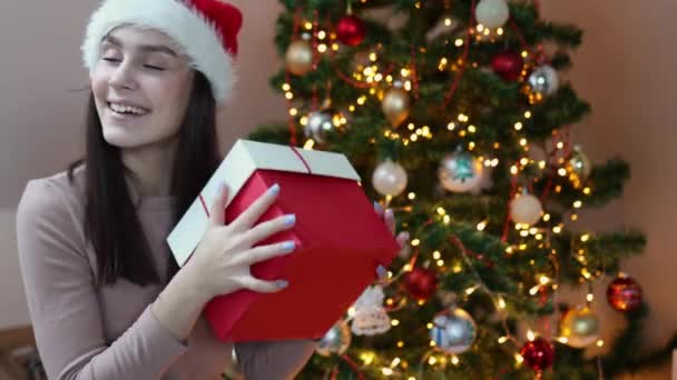 Dość biały szczęśliwy brunetka kobieta Santa kapelusz czerwony prezent pudełko ozdobione jodła — Wideo stockowe