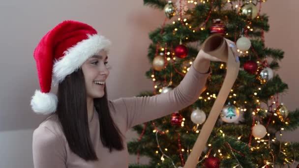 Morena caucásica mujer en rojo Santa sombrero de lectura Navidad lista de deseos carta — Vídeos de Stock