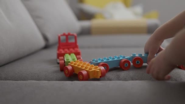 Baby child boy playing with colorful plastic bricks train on grey sofa at home — Stock Video
