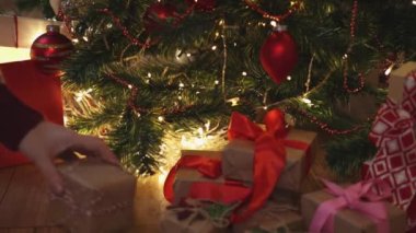 Kırmızı el işi hediye kutularını süslü Noel ağacı ışıklarının altına yerleştiriyor.