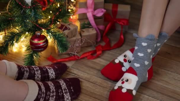 Duas mulheres par pernas em meias de Natal sentado sob caixa de presente de abeto decorado — Vídeo de Stock