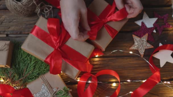 Mains féminines enveloppant cadeaux de Noël artisanat papier attachant ruban rouge arc — Video