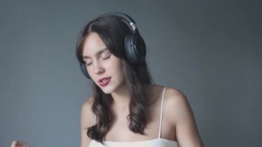 Mutlu, genç, esmer kız kulaklık takıyor, gülümsüyor, müzik dinliyor.