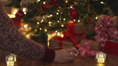 Süslü köknar ağacı hediyesinin altına ahşap çelenk koyuyor.