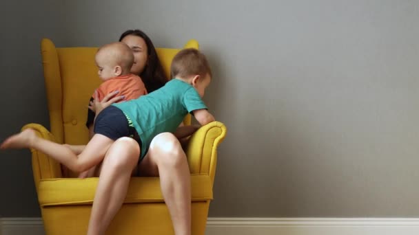 Zmęczona młoda matka siedzi zakłócać w fotelu z dwójką niegrzecznych dzieci — Wideo stockowe