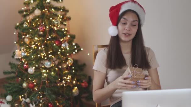 Jeune étudiante brune en rouge Santa chapeau streaming ordinateur portable montrant boîte cadeau — Video