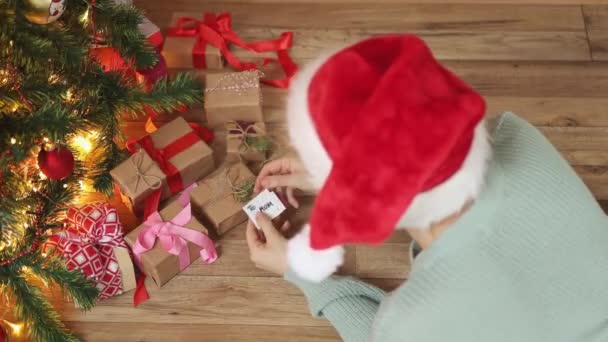 Psaní přání k Vánocům dárky žena červená čepice pod jedle strom dárky — Stock video