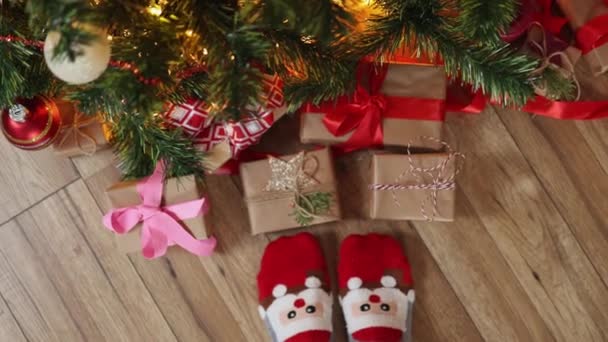 Pés em meias de Natal engraçadas Santa face chão de madeira sob caixas de presente de abeto — Vídeo de Stock