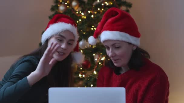 Yeşil Noel Baba şapkalı iki kadın Noel ağacında akıllı telefon kullanıyor. — Stok video