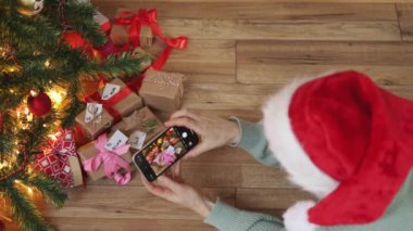Kadın kırmızı Noel şapkalı akıllı telefon köknar ağacının altında yeşil ekran hediye kutuları veriyor