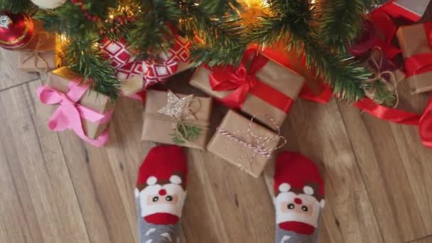 Pés em meias de Natal engraçadas Santa face chão de madeira sob caixas de presente de abeto — Vídeo de Stock