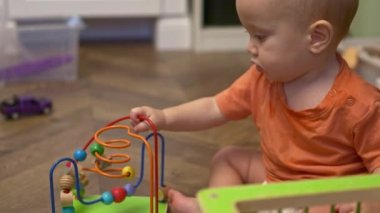 Turuncu tişörtlü şirin bebek tahta daireli boncuk labirent eğitim oyuncağı oynuyor. 