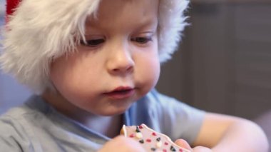 Yakın plan portre 3 yaşındaki çocuk Noel Baba kırmızı şapkalı Noel kurabiyesi yiyor. 