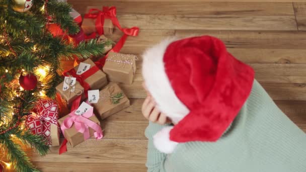 Alto ângulo vista pessoa vermelho Santa chapéu chão de madeira sob árvore de Natal caixa de presente — Vídeo de Stock