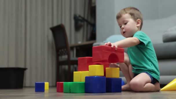 Mały chłopiec budynek garaż wieża z kolorowych plastikowych kostek bloków na podłodze — Wideo stockowe