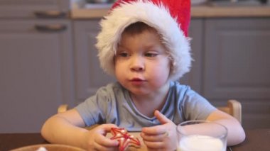 Küçük beyaz çocuk 3 yıldır Noel Baba kırmızı şapka çiğneyen ev yapımı kurabiye yiyor. 