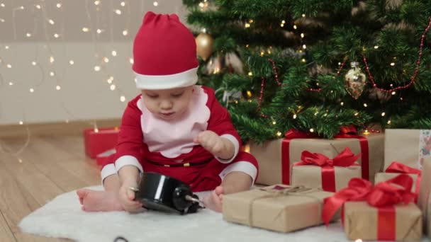 Dziecko maluch dziecko w stroju Mikołaja siedzi ozdobione jodły rzemieślnicze pudełka upominkowe — Wideo stockowe