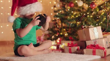 Küçük çocuk yeşil tişört ve kırmızı Noel Baba şapkası hediye ile köknar ağacının altında.