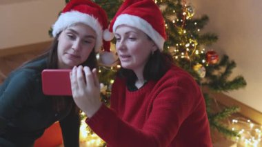 İki kadın kırmızı Noel Baba yeni yılda akıllı telefon kullanarak görüntülü konuşma yapıyorlar.