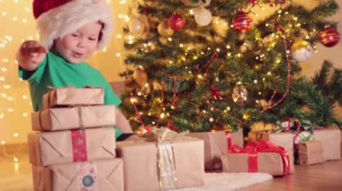 Küçük çocuk yeşil tişört ve kırmızı Noel Baba şapkası hediye ile köknar ağacının altında.