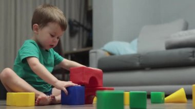 Küçük çocuk yerde renkli plastik bloklardan kule garajı inşa ediyor.