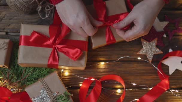 Mains féminines enveloppant cadeaux de Noël artisanat papier attachant ruban rouge arc — Video