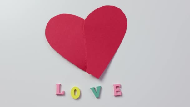 Prsty oddělující dvě poloviny červeného papíru srdce na bílém slově milostná písmena — Stock video