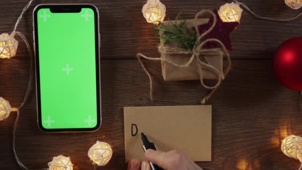 Концепція різдвяних пожертвувань: рукопис подарункової картки та смартфона на зеленому екрані — стокове відео
