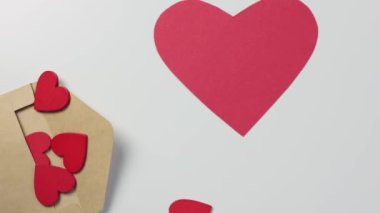 Beyaz masanın içinde bir sürü kırmızı kalp olan bir zarf büyük kağıt bir kalbe düştü.