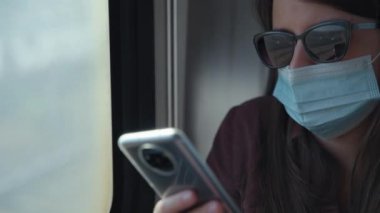 Maskeli kadın telefonla trene biniyor.